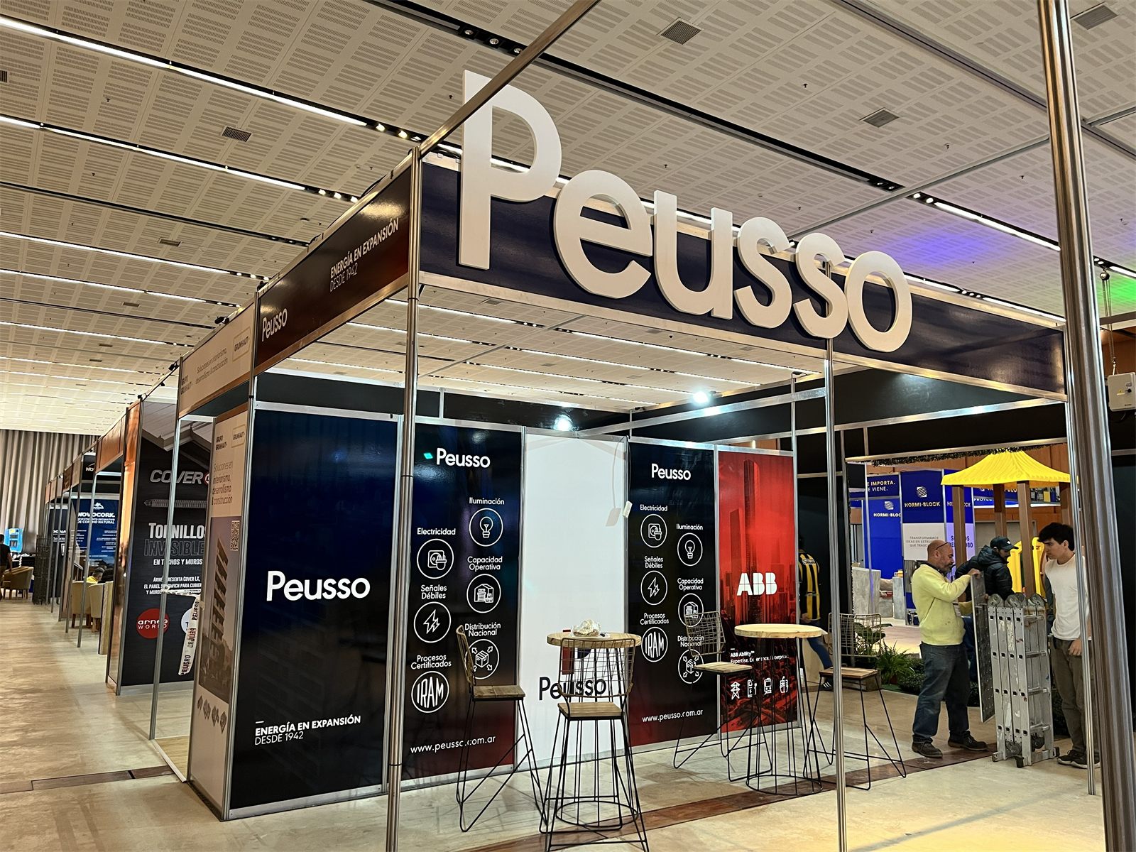 Stand de Peusso en una exposición, con paneles de sus servicios y el nombre en letras corpóreas